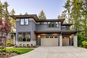 Single family home exterior featuring gray wood siding, stone columns, and two garages.